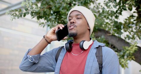 African american man talking on smartphone while commuting with headphones and backpack