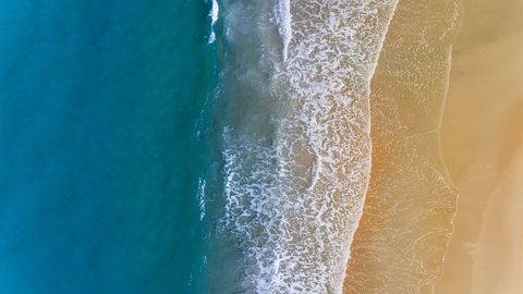 Aerial turquoise ocean meeting golden sand shoreline with foamy surf and gentle waves