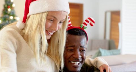 Diverse Couple Embracing on Couch with Holiday Headwear