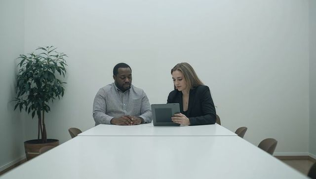 Two colleagues reviewing tablet in minimalist conference room during business meeting