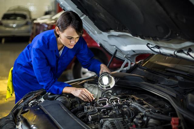 Female mechanic examining a car engine with lamp in repair garage