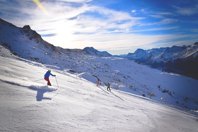 Groups of skiers descending a snowy mountain slope under a bright, sunny sky. Suitable for travel and adventure advertisements, winter sports promotions, tourism brochures, and outdoor recreation features.