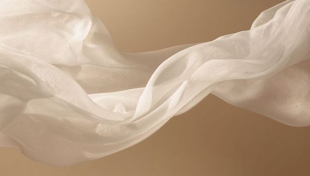 Ethereal sheer fabric flowing over warm beige backdrop showing fine weave and texture