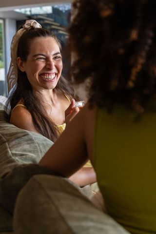 Sunlit laughter: diverse female friends laughing and chatting on modern sofa
