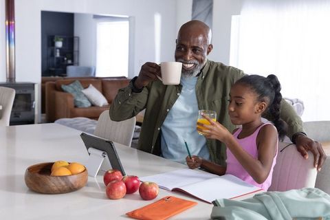 African american mature man helping child with homework at kitchen island over morning coffee