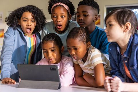 Multicultural children gathering around tablet watching screen for collaborative learning