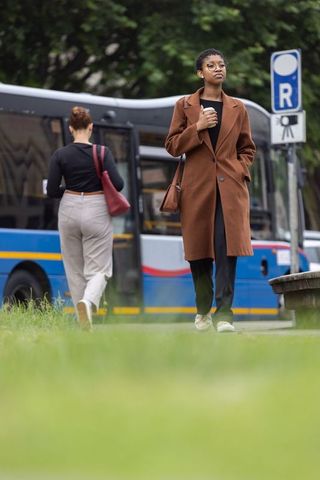 Urban commuter african american woman walking past bus holding coffee cup in brown coat