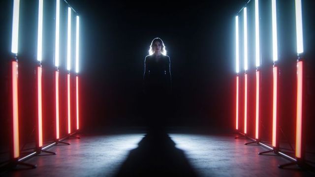 Woman standing backlit between symmetrical red and white led columns, silhouette drama