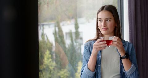 Woman Holding Red Tea Looking Out Window in Thoughtful Moment