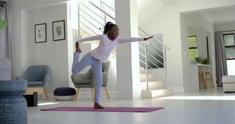 Young african girl practicing yoga at home on purple mat balancing in bright living room