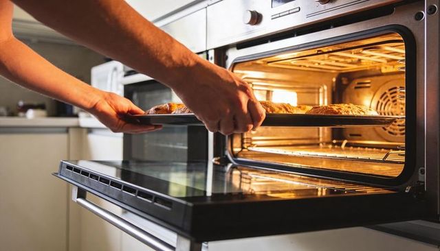 Home baking hands placing golden artisan loaves into stainless built-in oven