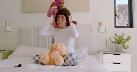 Mother and daughter bonding with hair styling and teddy bear