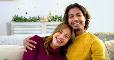Couple leaning together smiling on sofa during cozy holiday lights and warm decor