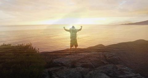 Hiker Raising Arms Overlooking Tranquil Sea at Sunset