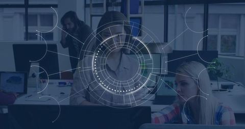 Collaborating team leaning around monitors with futuristic HUD overlay in modern office