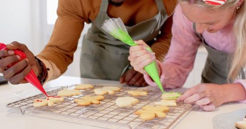Joyful friends decorating sugar cookies with icing in modern kitchen