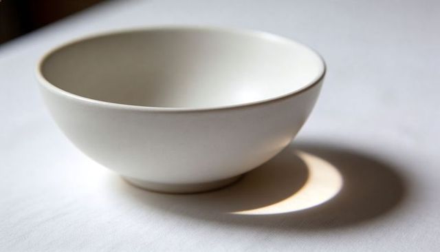 Minimalist white ceramic bowl with soft rim highlight and crescent shadow on textured linen