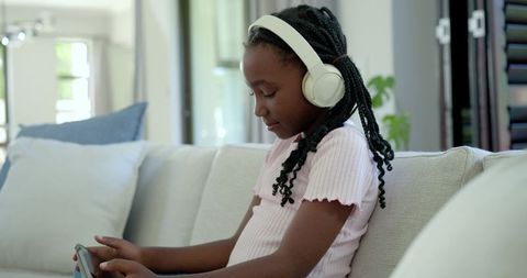 African american girl wearing headphones using tablet on sofa, enjoying screen time