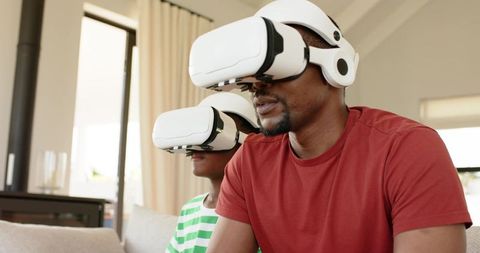 Father and son wearing vr headsets on sofa exploring virtual reality together