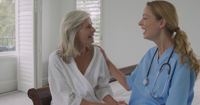 Senior Caucasian woman receives care from a nurse at home. They share a moment of joy during a health check-up, highlighting compassionate care.