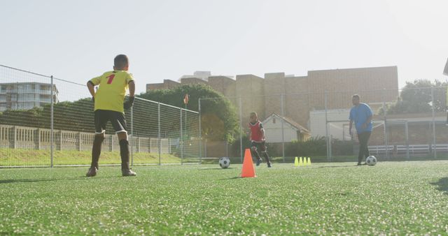 Three boys participating in a soccer training session, running around cones on a sunny day. This image is ideal for promoting youth sports programs, athletic training camps, or school team advertisements. It emphasizes teamwork, skill development, and healthy, active lifestyles for children.
