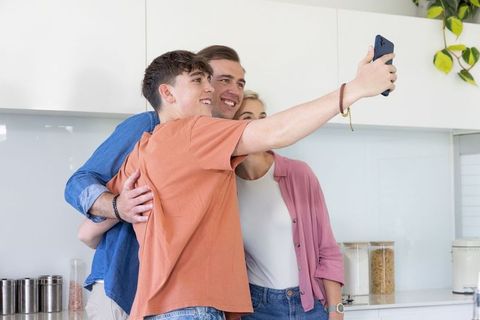 Family taking smartphone selfie in bright modern kitchen smiling and hugging for lifestyle use
