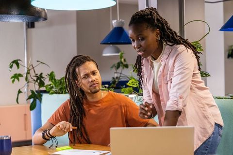 African american coworkers collaborating over laptop in modern pastel office nook planning