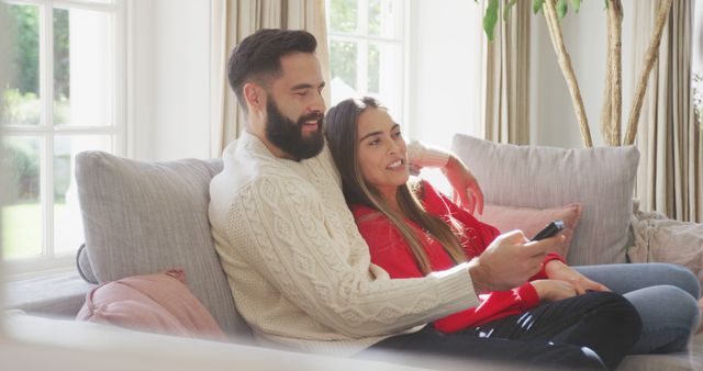 Couple sitting on sofa together, enjoying relaxed time watching TV. Ideal for themes of leisure, domestic life, casual comfort, and togetherness. Perfect for illustrating family life, relationship dynamics, or home lifestyle content.