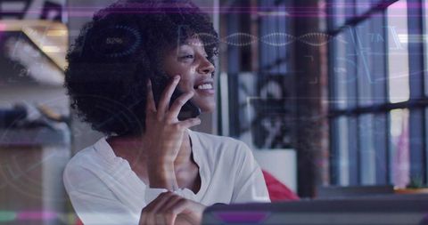 Smiling businesswoman talking on phone while viewing data visualizations in modern office