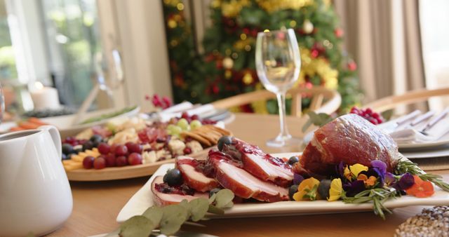 Outdoor sunlight illuminates an elegantly set table with a Christmas-themed meal, featuring roasted meat adorned with berries and flowers. A decorated Christmas tree is visible in the background, adding to the festive atmosphere. Ideal for holiday marketing materials, cooking blogs, and festive invitations.