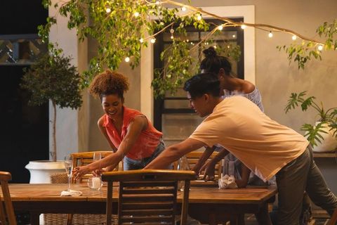 Friends gathering outdoors at night preparing table with wine glasses and string lights