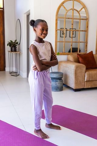 African american girl standing confidently on purple yoga mats wearing lavender joggers
