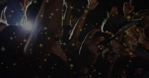 Silhouetted fan recording concert with smartphone, backlit crowd and sparkling light effects