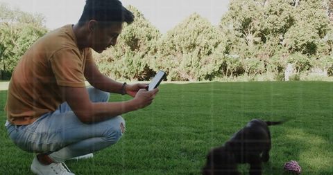 Man capturing playful puppy with tablet in sunlit backyard exploring rope toy
