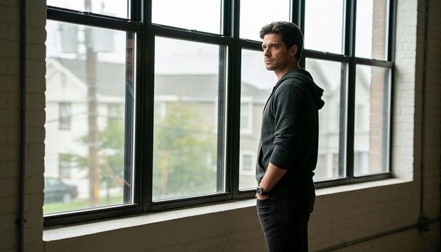 Contemplative man standing by large steel loft windows gazing outside urban neighborhood