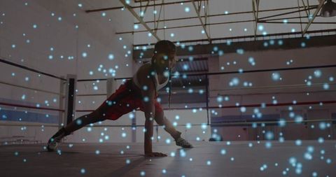 Balancing woman performing one-handed plank in boxing ring with blue particle lights