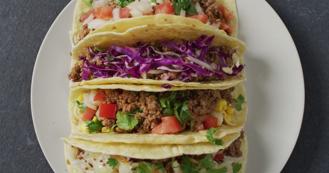 Three tacos filled with seasoned ground beef and fresh vegetables such as diced tomatoes, shredded cabbage, corn, and coriander, arranged on a white plate. Ideal for promoting restaurants, food blogs, Mexican culinary content, or cooking recipes.