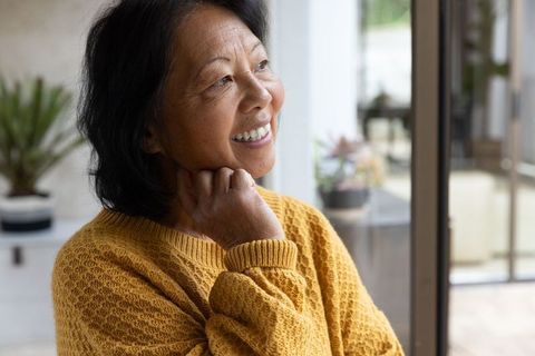 Serene Senior Woman Looking Out Glass Door with Hand on Chin