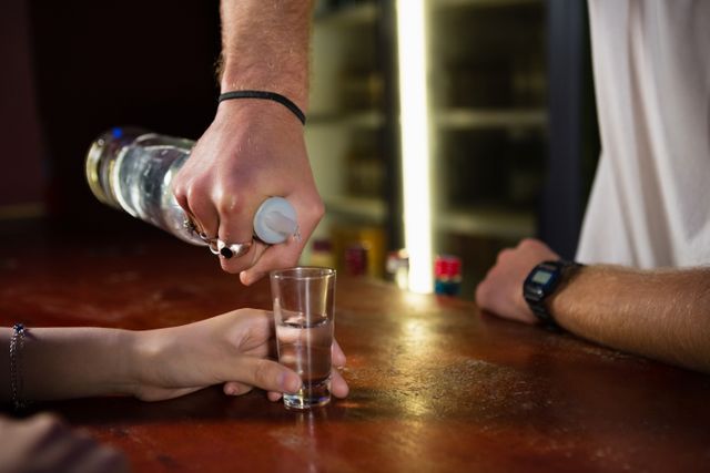 Bartender pouring tequila into a shot glass for a customer at a bar counter. Ideal for use in articles or advertisements related to nightlife, bars, alcohol service, hospitality industry, and social gatherings.