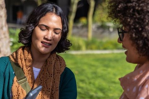 Multicultural young women checking smartphone together in sunlit park, casual conversation