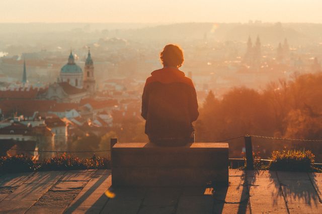 Person sitting on bench overlooking city during sunset. Suitable for use in themes of travel, tourism, meditation, inner peace, solitude, reflection, adventure.