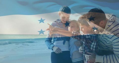 Honduran family enjoying beach day pointing toward horizon, parents embracing children