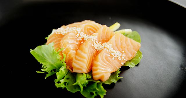 Slices of fresh salmon sashimi are delicately placed on a bed of crisp lettuce, garnished with sesame seeds. Sashimi is a popular Japanese delicacy consisting of fresh, raw fish, often enjoyed for its flavor and texture.