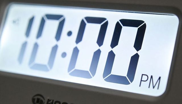 Close-up backlit digital alarm clock displaying 10:00 pm glowing lcd minimal night scene