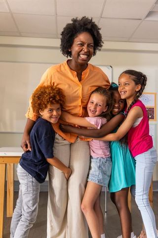 African american teacher hugging diverse smiling elementary students, warm classroom connection