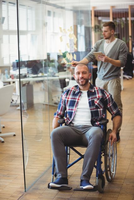 Portrait of smiling handicap businessman with colleague in background at creative office