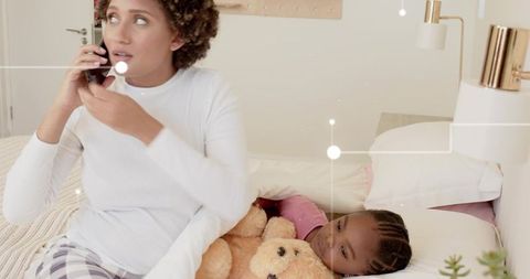 Mother talking on phone while child cuddling teddy in cozy minimalist bedroom nighttime family care