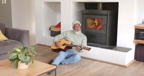 Elderly Man Playing Acoustic Guitar Near Cozy Fireplace at Home
