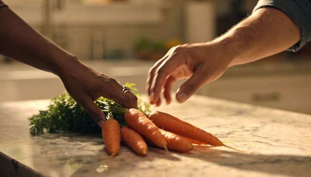 Couple arranging fresh carrots on marble countertop, hands prepping market produce