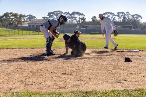Senior players sliding into home plate during competitive baseball play, catcher blocking